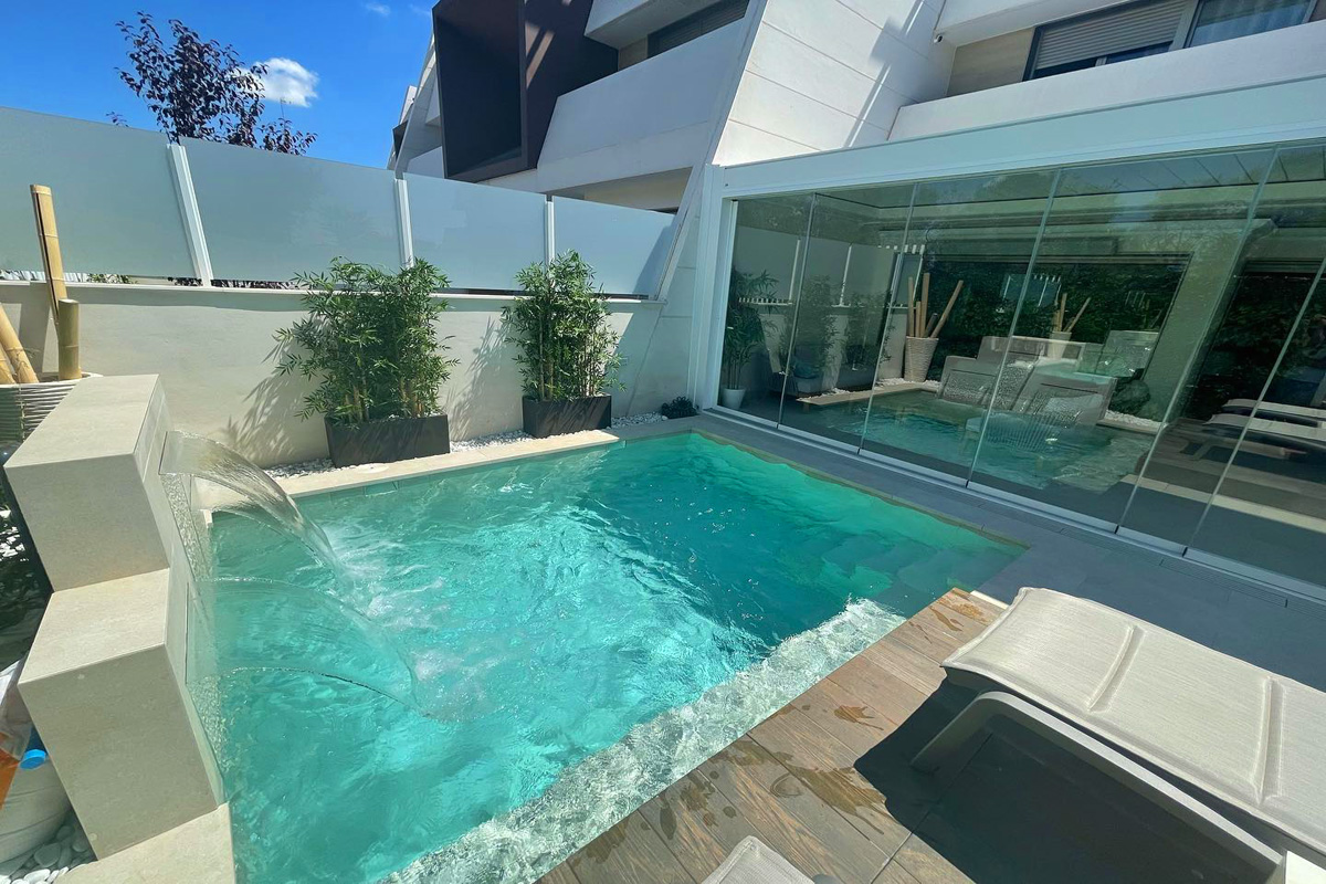 Pequeña piscina exterior en terraza con cascada de obra decorada con bambú con porche de casa moderna cubierto y cerrado con puertas de cristal
