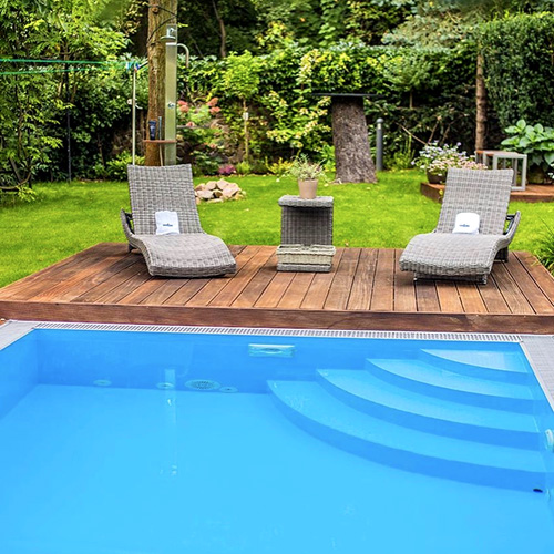 piscina lamina armada color azul con tarima de madera y escalera de obra esquinera tipo tarta en jardín con vegetación
