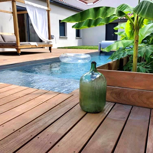piscina lamina armada color gris oscuro en terraza pequeña con suelo entarimado de madera cesped y vegetación tropical