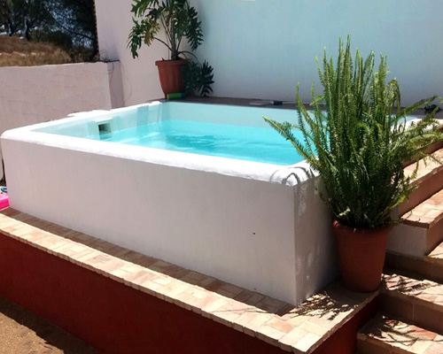 piscina ibicenca de poliester color blanca rectangular Triana con muro de piedra blanco encalado como revestimiento y escaleras de obra en patio de casa