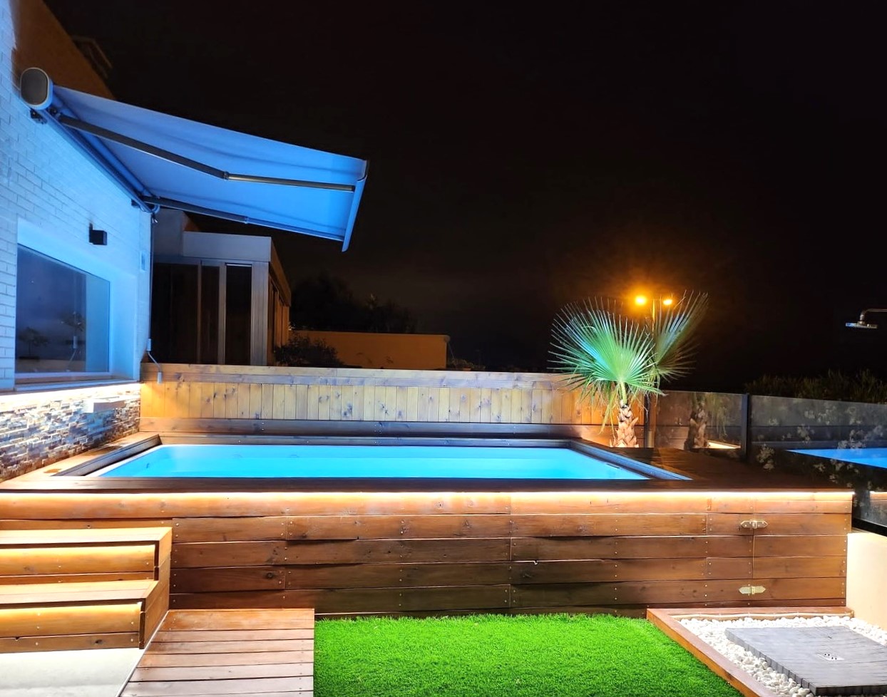 piscina luna de 4 metros de fibra y poliester elevada y revestida con vigas de madera tratada en jardin de noche